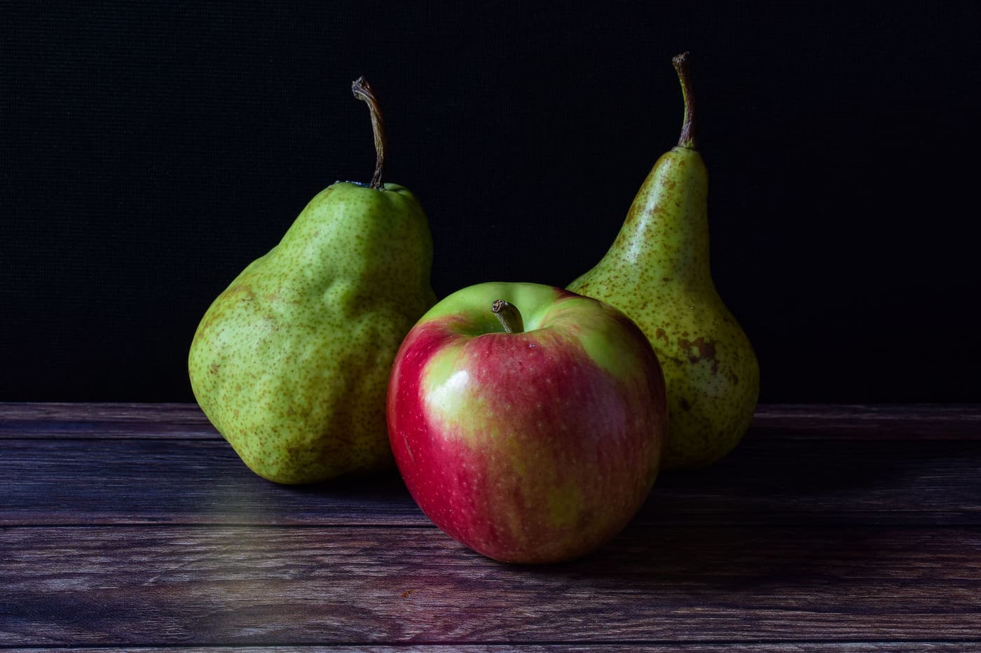 An apple and two pears on a dark wooden table